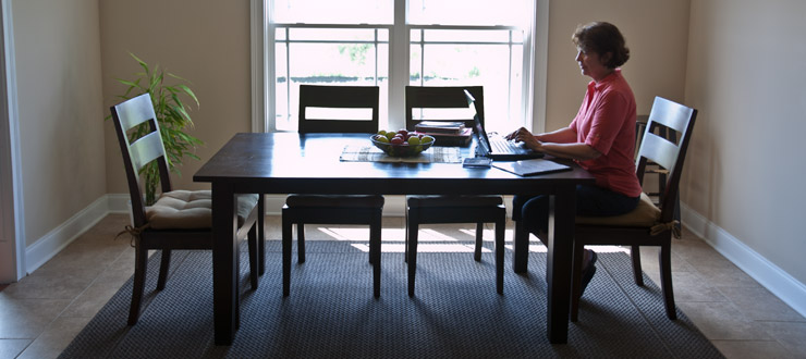 Woman sitting at dining room table working on laptop