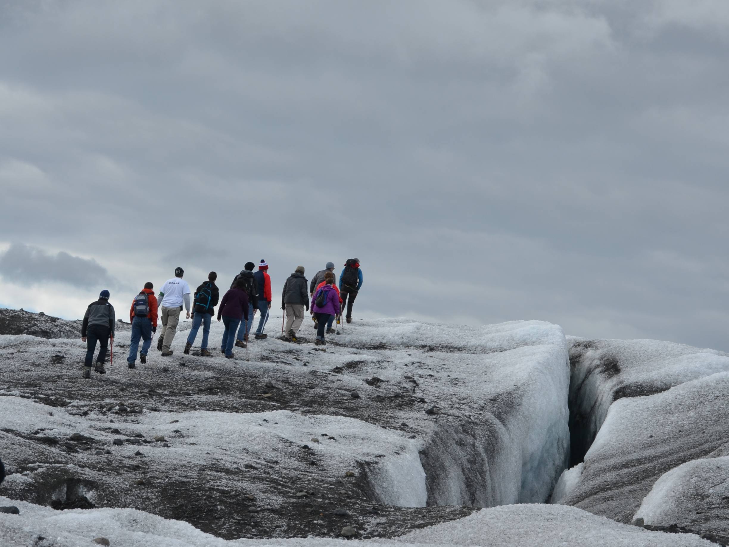 A line of students hike on a snowy surface.