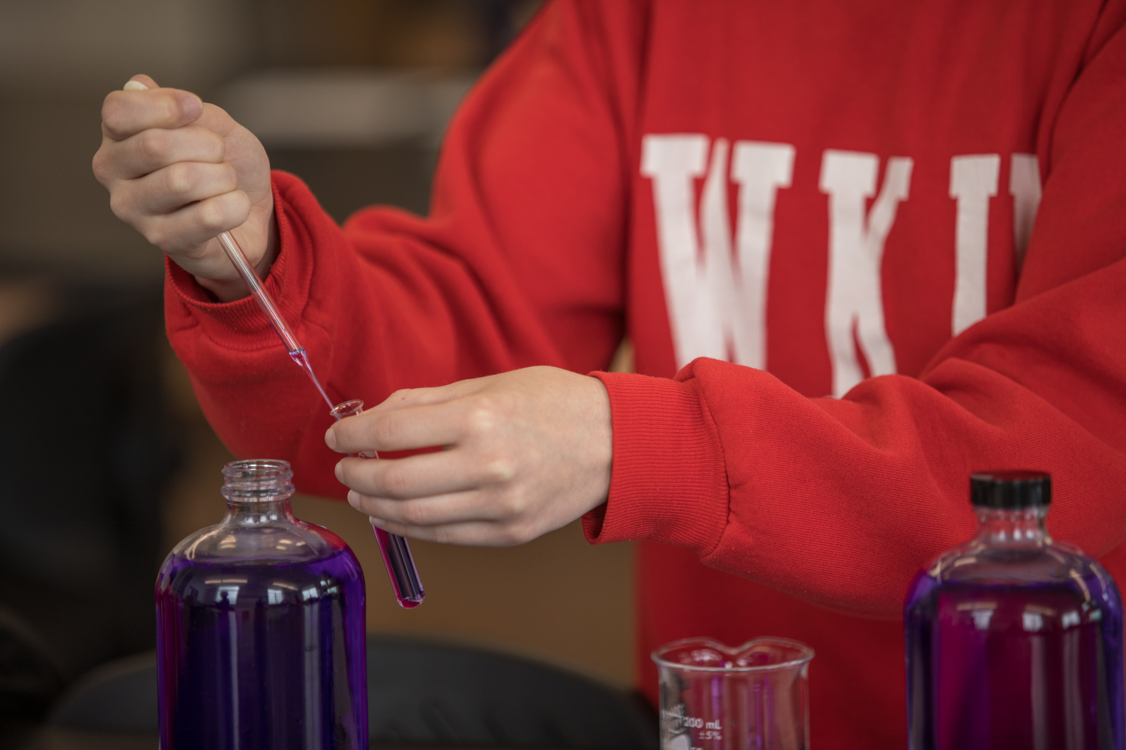 A student uses a dropper to transfer purple liquid from a bottle to a test tube.