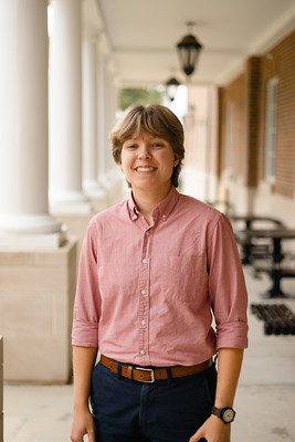 young female student in pink button down shirt and dark pants standing in front of a column for a headshot