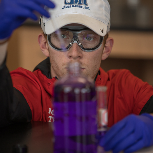 A WKU student wearing lab goggles uses a dropper to get purple liquid from a bottle in a Chemistry lab.