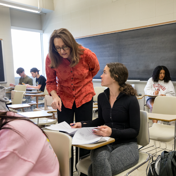 A Mathematics professor talks to a student in a classroom.