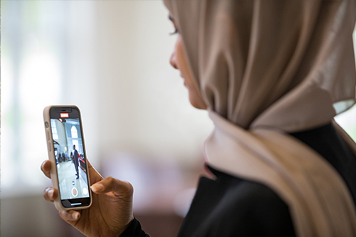 Individual wearing a hijab using a smartphone to record video at a campus event