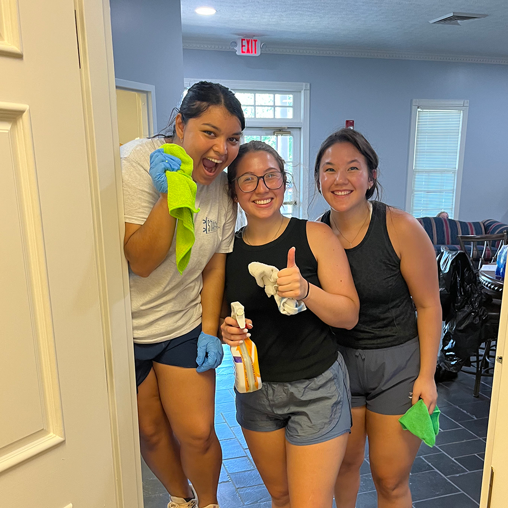 three students posing for a photo with cleaning supplies in their hands