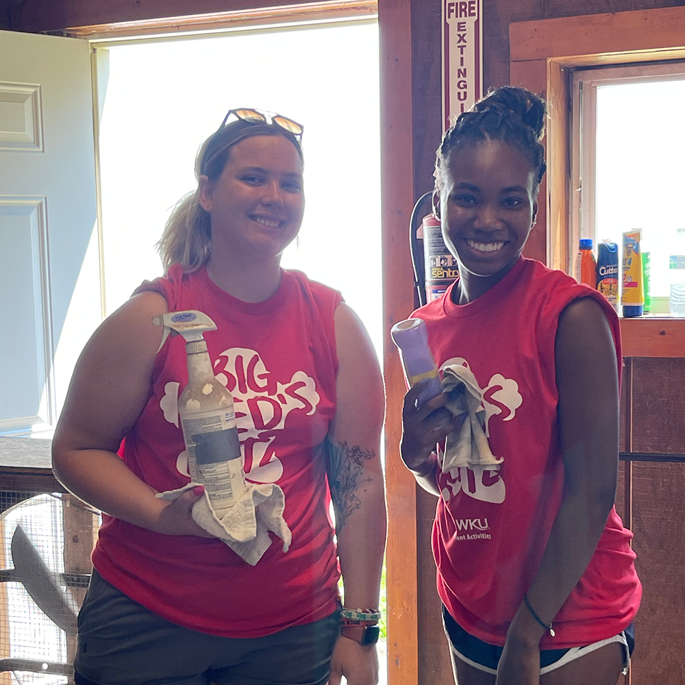 Students posing for a photo while holding cleaning supplies