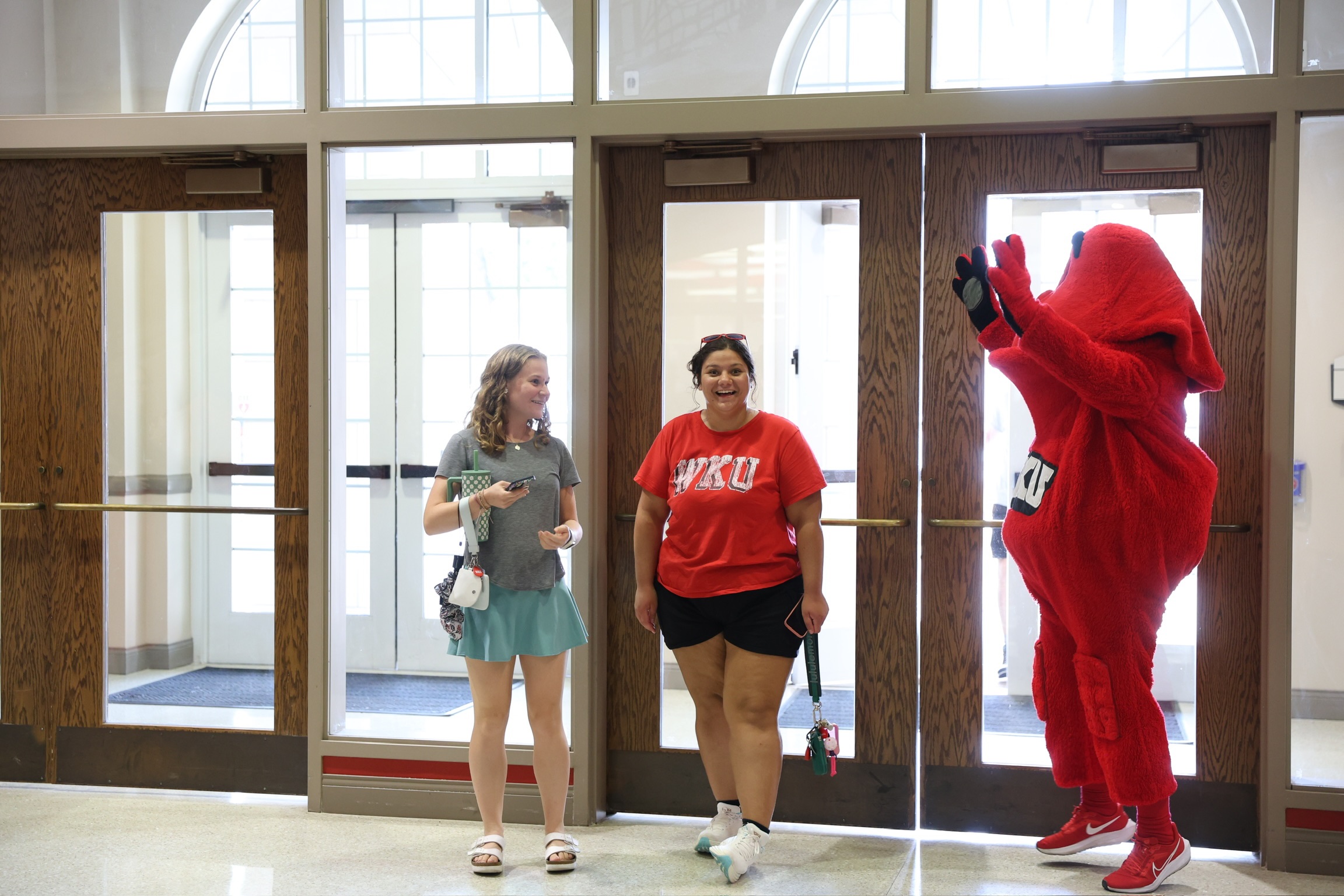 Big Red is jumping to greet two students