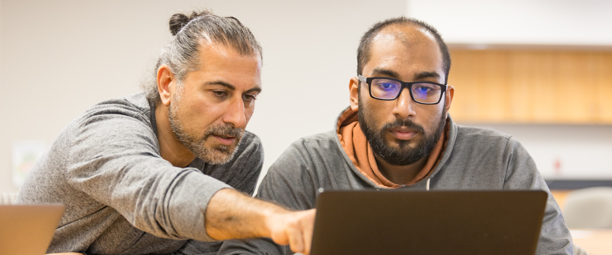 A mathematics professor works with a student and points to something on the student's laptop.